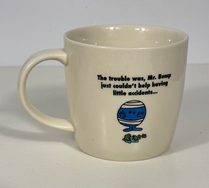 An off-white ceramic mug featuring a black printed quote and a blue-and-white Mr. Bump cartoon illustration with a small green frog below, set against a plain light background.