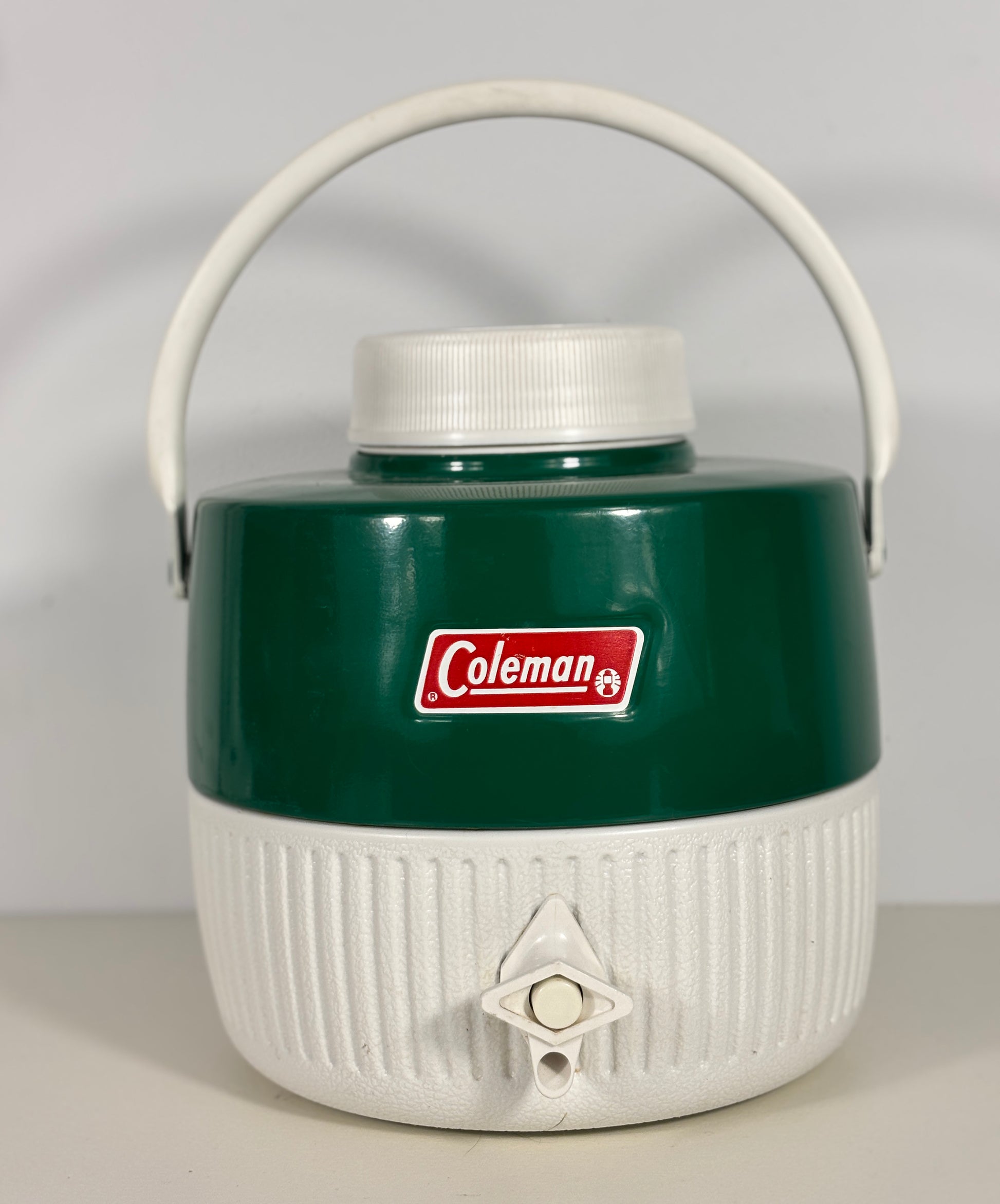Green and white Coleman cooler with a handle on a light gray background