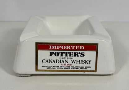 A white ceramic potter's ashtray featuring a printed label for 'Potter's Canadian Whisky' on the front.