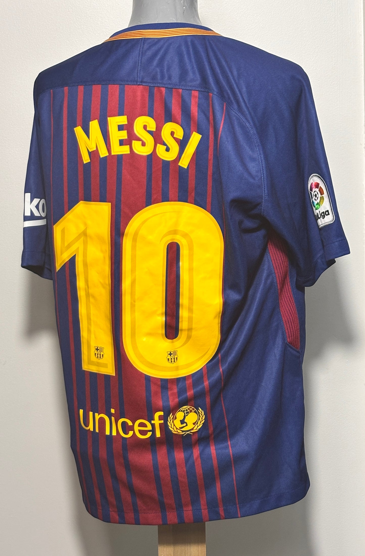 Back view of a blue and red striped FC Barcelona soccer jersey with 'MESSI' and number '10' in yellow, displayed on a mannequin torso.