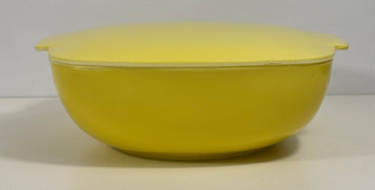 A bright yellow plastic bowl with a matching lid, photographed against a neutral light gray background.