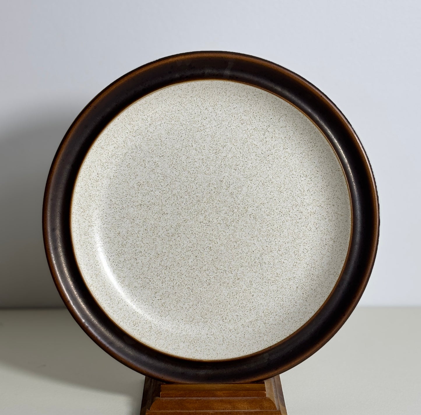 Round stoneware plate with brown rim on a stand against a light background