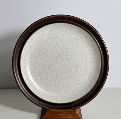 Round stoneware plate with brown rim on a stand against a light background