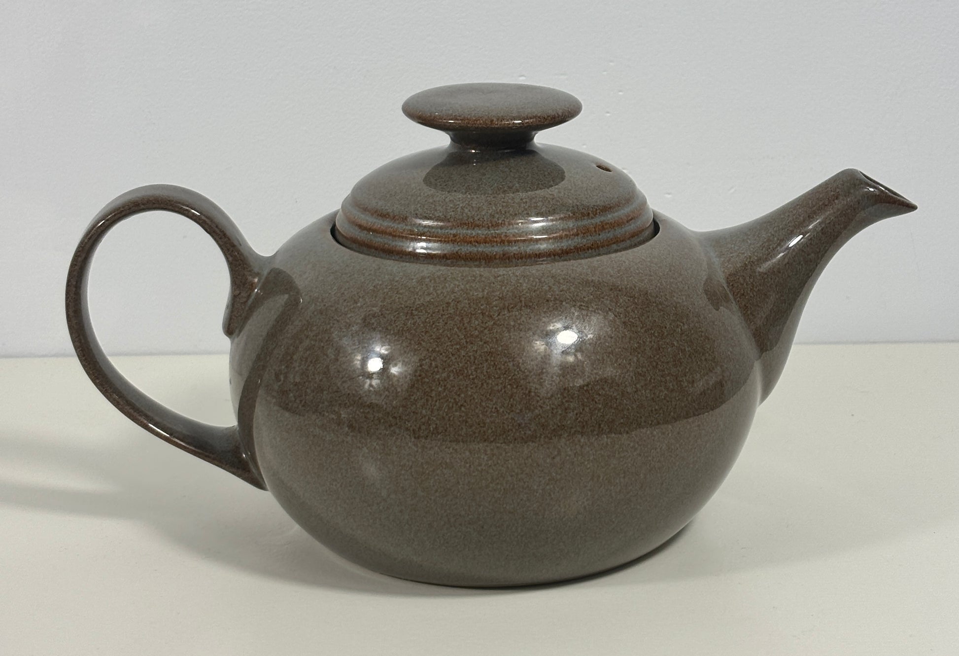 A brown speckled ceramic teapot with a matching lid, shown on a plain light background.