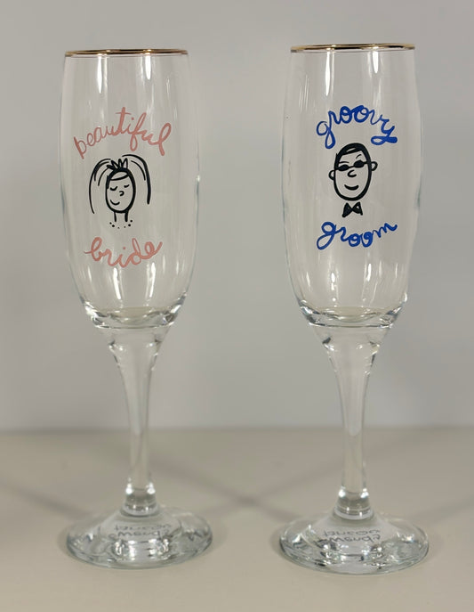 Two champagne flutes with 'beautiful bride' and 'groovy groom' text on a plain background