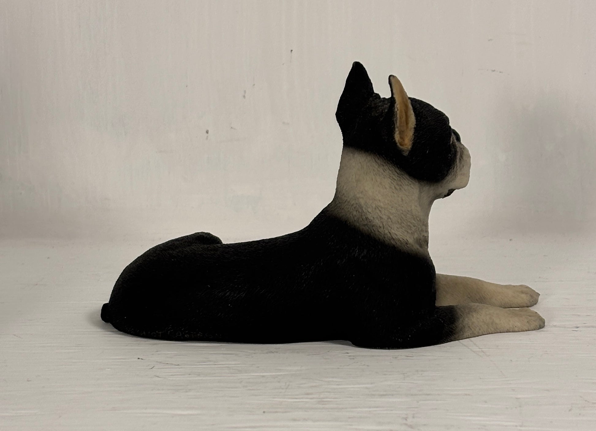 Black and white dog figurine lying on a light wooden floor against a plain white wall.