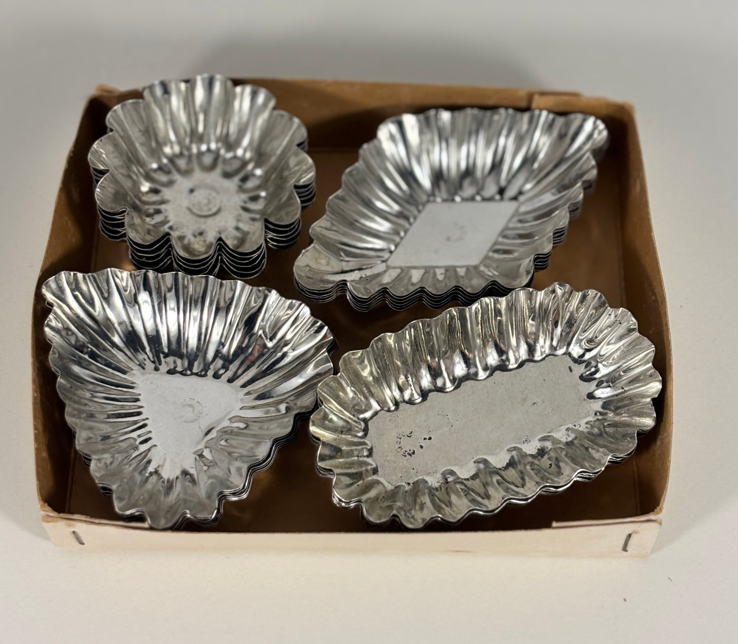 Set of silver metal tart tins in a cardboard box on a white background