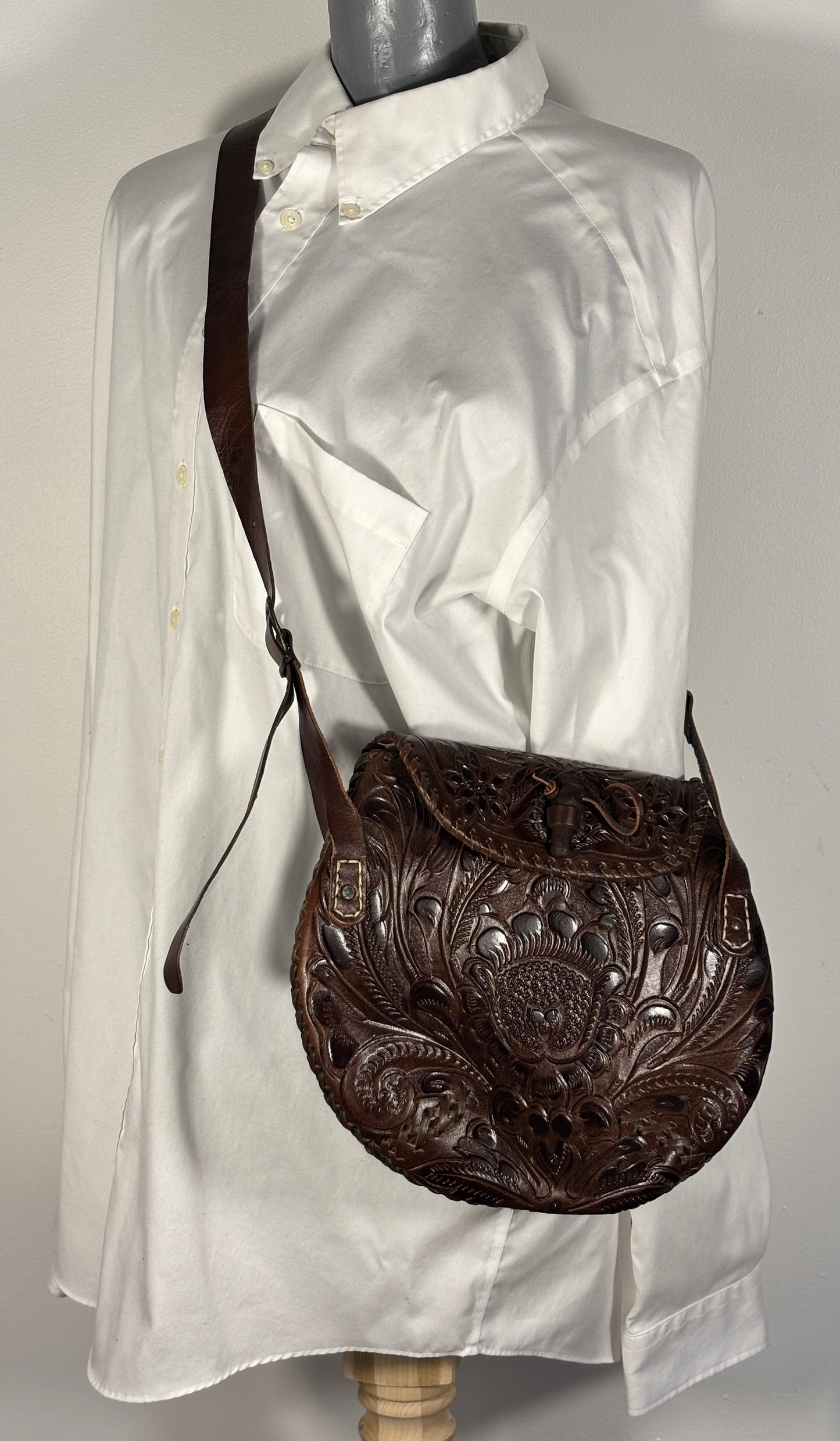Brown leather handbag with intricate designs on a mannequin wearing a white shirt.