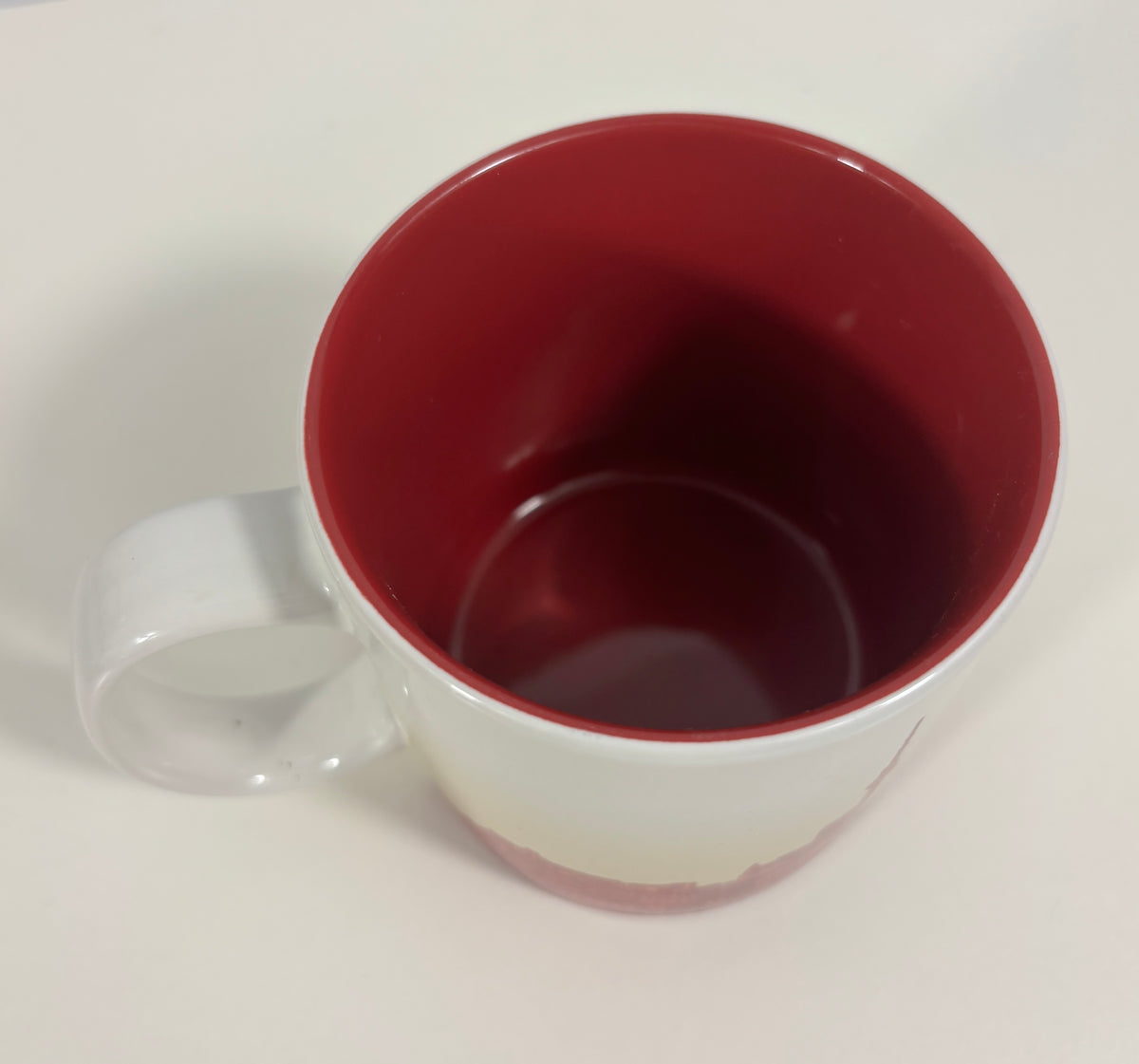 A white ceramic mug with a deep red interior, shown from a top-down angle on a plain white surface.