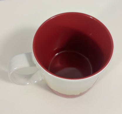 A white ceramic mug with a deep red interior, shown from a top-down angle on a plain white surface.