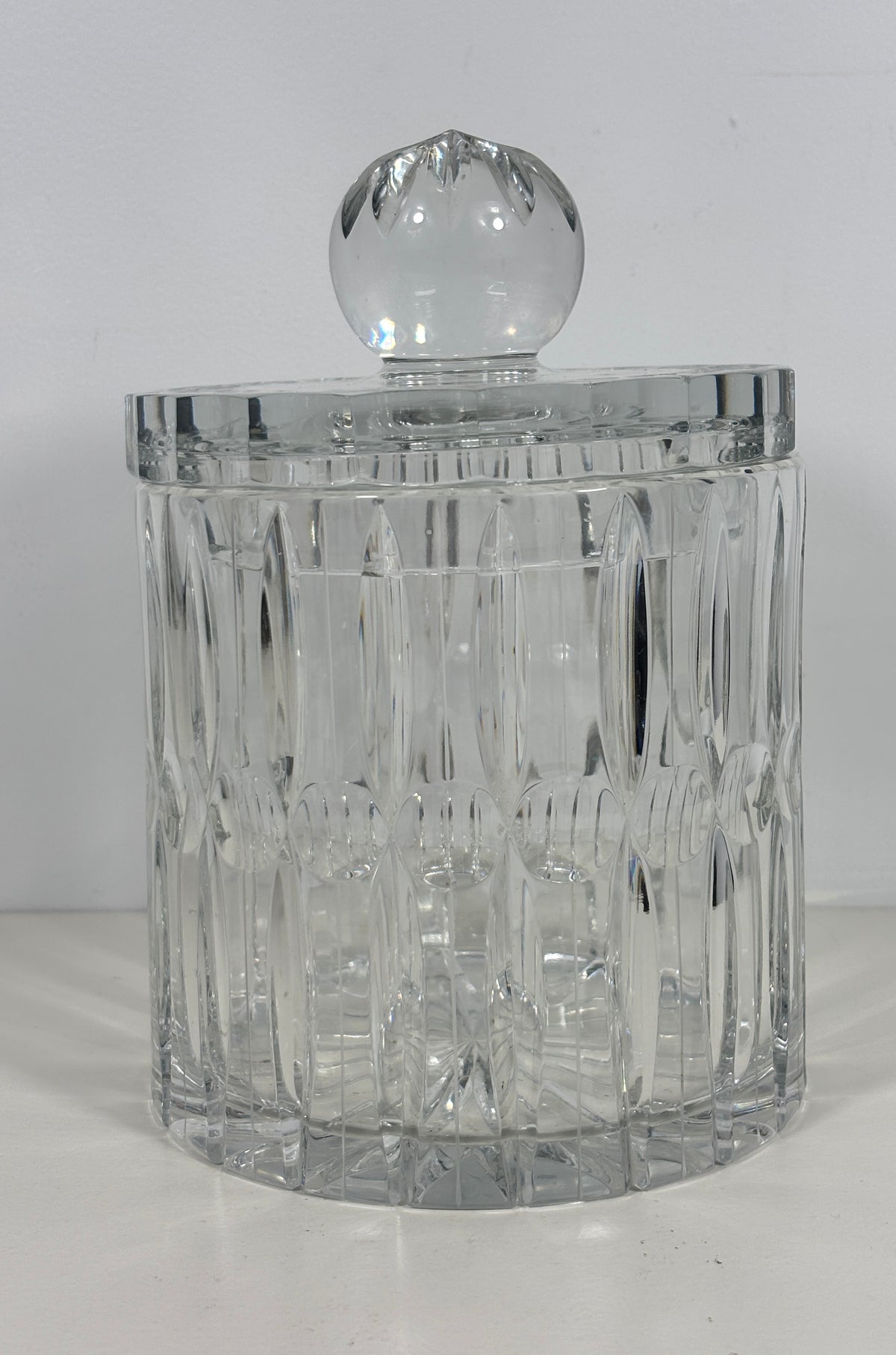 A clear cut-crystal or glass lidded container with a faceted round top, photographed against a plain light background.