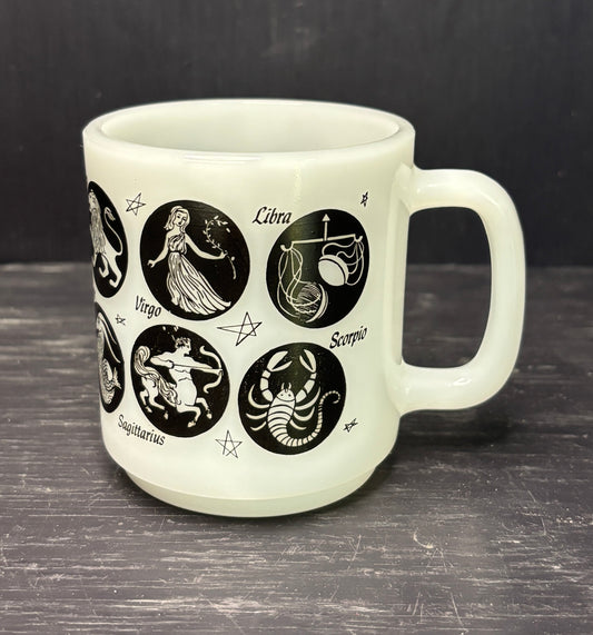 White mug with black zodiac illustrations on a dark surface