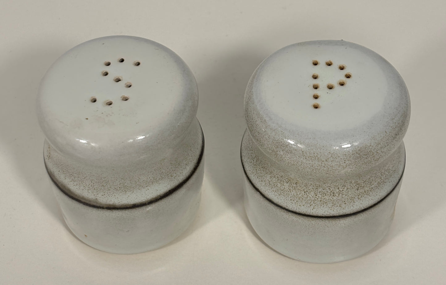 A pair of vintage ceramic shakers with a speckled off-white glaze and dark brown bands, shown on a plain light background.