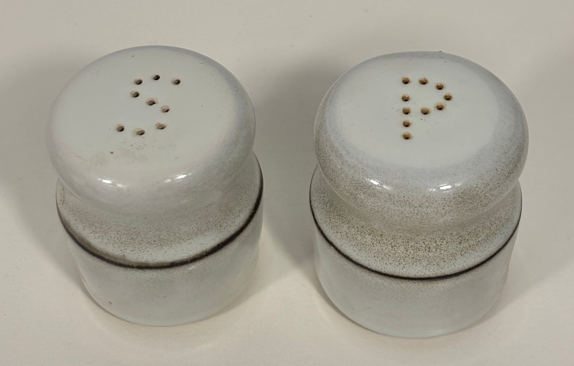 A pair of vintage ceramic shakers with a speckled off-white glaze and dark brown bands, shown on a plain light background.