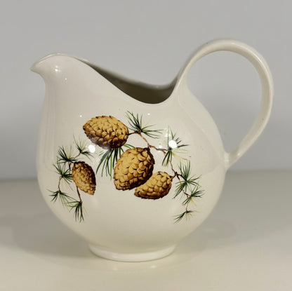 White ceramic pitcher with pine cone and branch design on a plain background