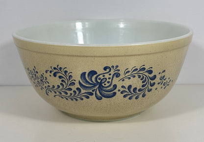 A vintage mixing bowl with a speckled beige exterior decorated with a blue floral scroll pattern, and a glossy white interior.