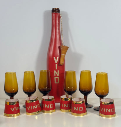 A vintage-style wine set featuring a tall red bottle-shaped decanter with 'VINO' printed vertically, alongside eight amber-tinted goblets and six matching red-and-gold paper cups, all arranged on a white surface against a light gray background.