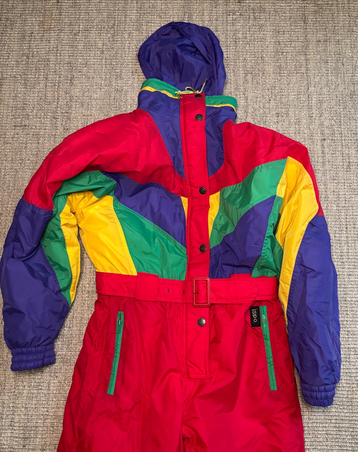 Colorful snowsuit with red, blue, yellow, and green sections on a textured surface.