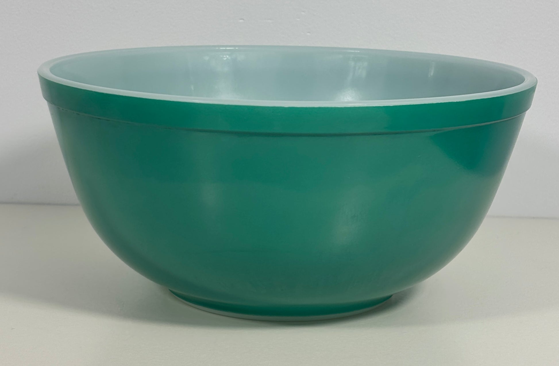 A vintage green glass mixing bowl with a lighter mint-green interior, photographed against a neutral light gray background.