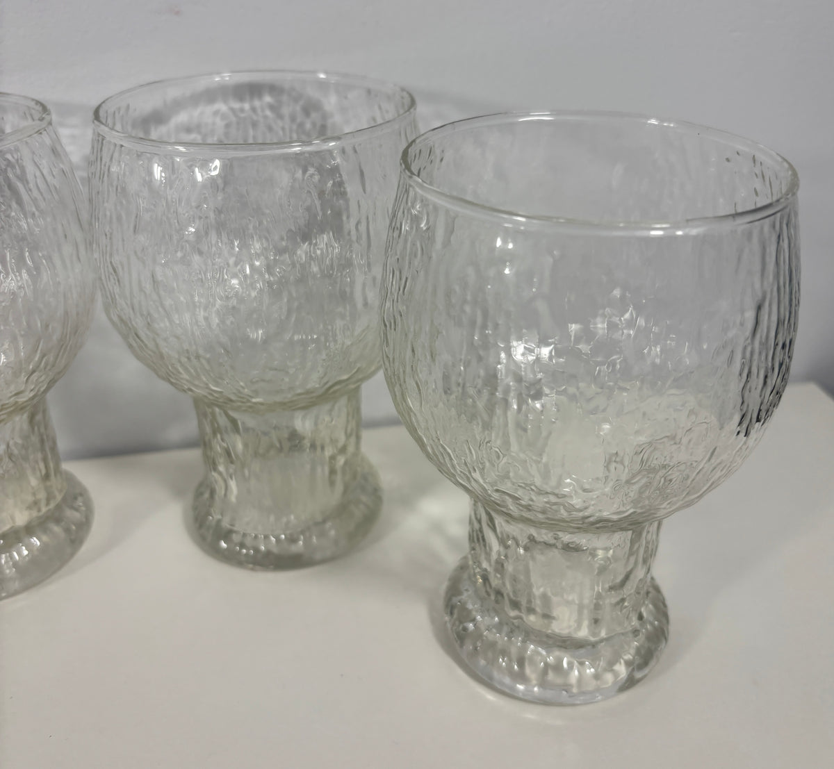 Three clear textured glass goblets with pedestal bases, shown on a white surface against a light gray background.