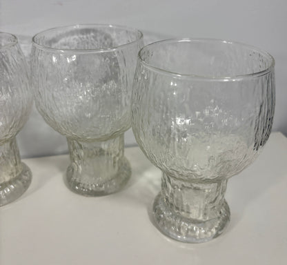 Three clear textured glass goblets with pedestal bases, shown on a white surface against a light gray background.