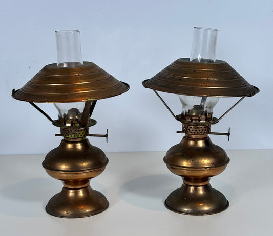 A pair of vintage brass oil lamps with clear glass shades, displayed side-by-side against a light blue background.