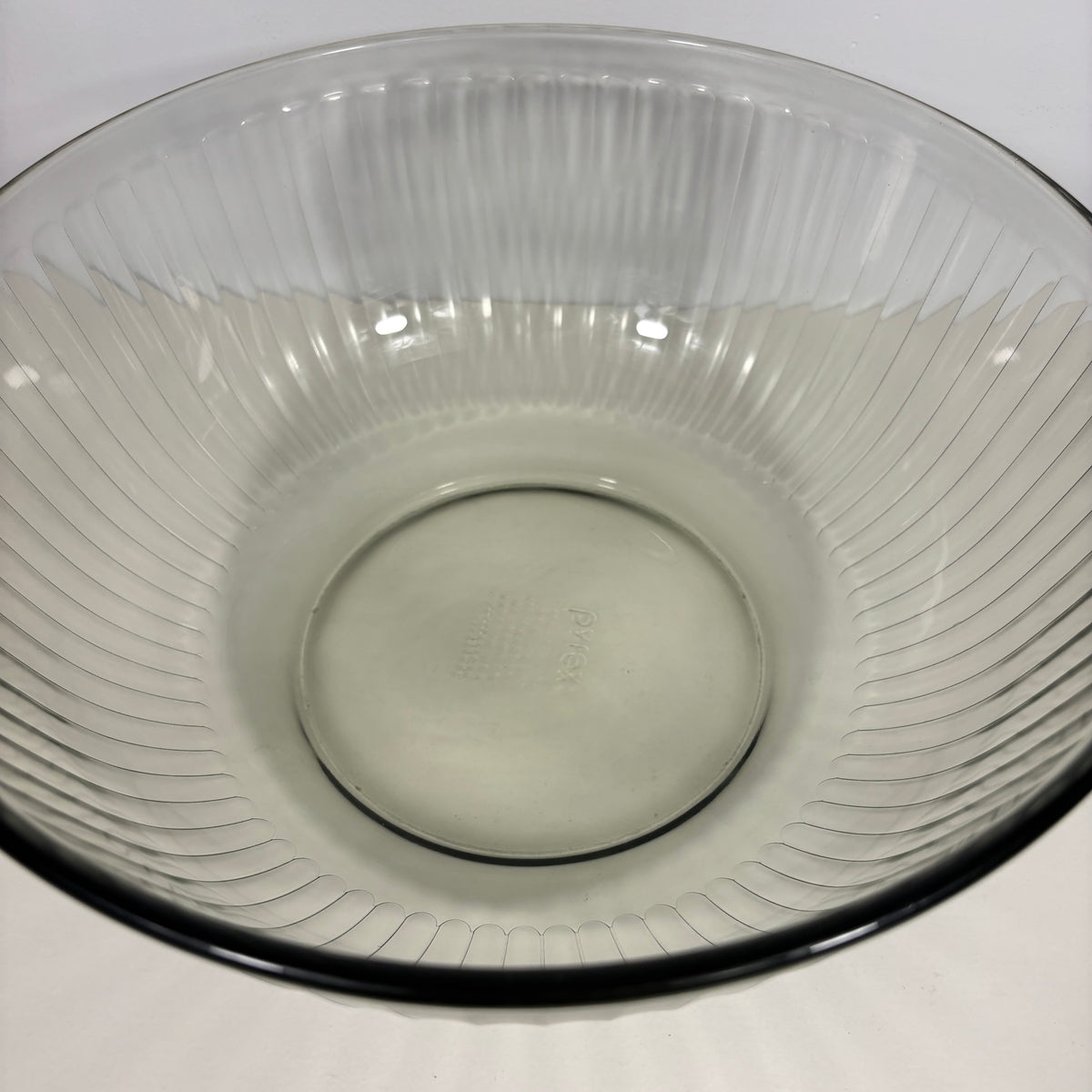 A clear ribbed glass mixing bowl with a flared rim and a dark rim, photographed from a top-down angle on a white surface.