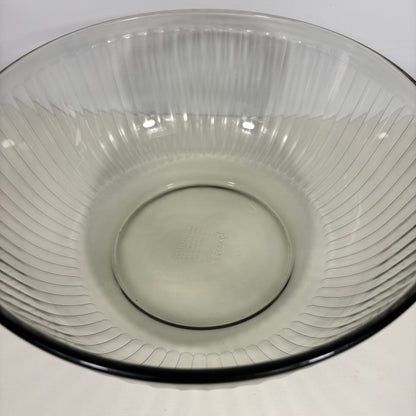 A clear ribbed glass mixing bowl with a flared rim and a dark rim, photographed from a top-down angle on a white surface.