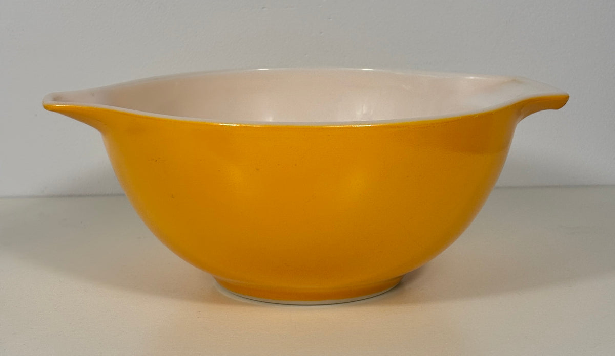 A vintage yellow glass mixing bowl with a cream-colored interior and small side handles, photographed against a neutral light gray background.