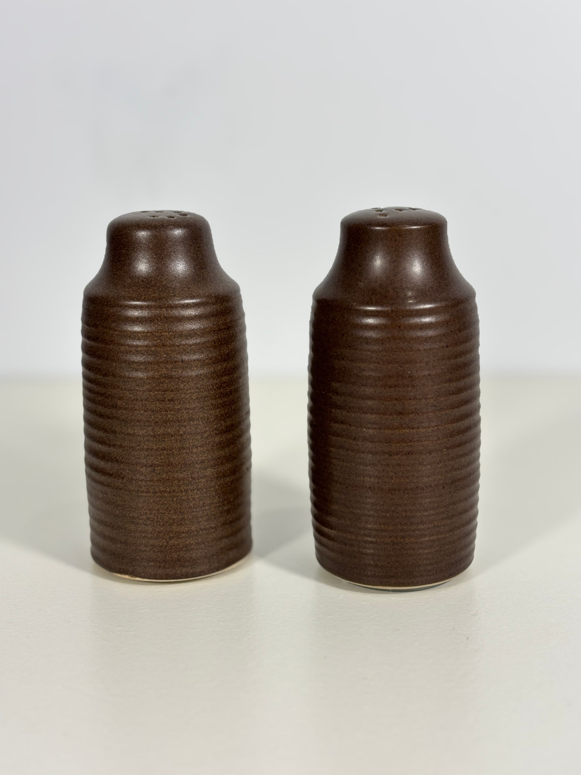 Two brown ribbed ceramic salt and pepper shakers on a white background