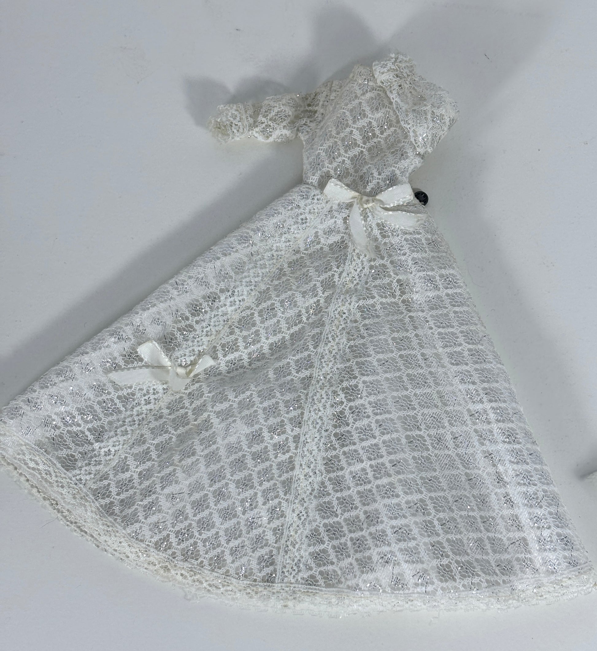 A white lace dress or capelet with a grid pattern and small ribbon bows, laid flat on a light gray background.