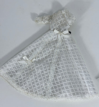 A white lace dress or capelet with a grid pattern and small ribbon bows, laid flat on a light gray background.