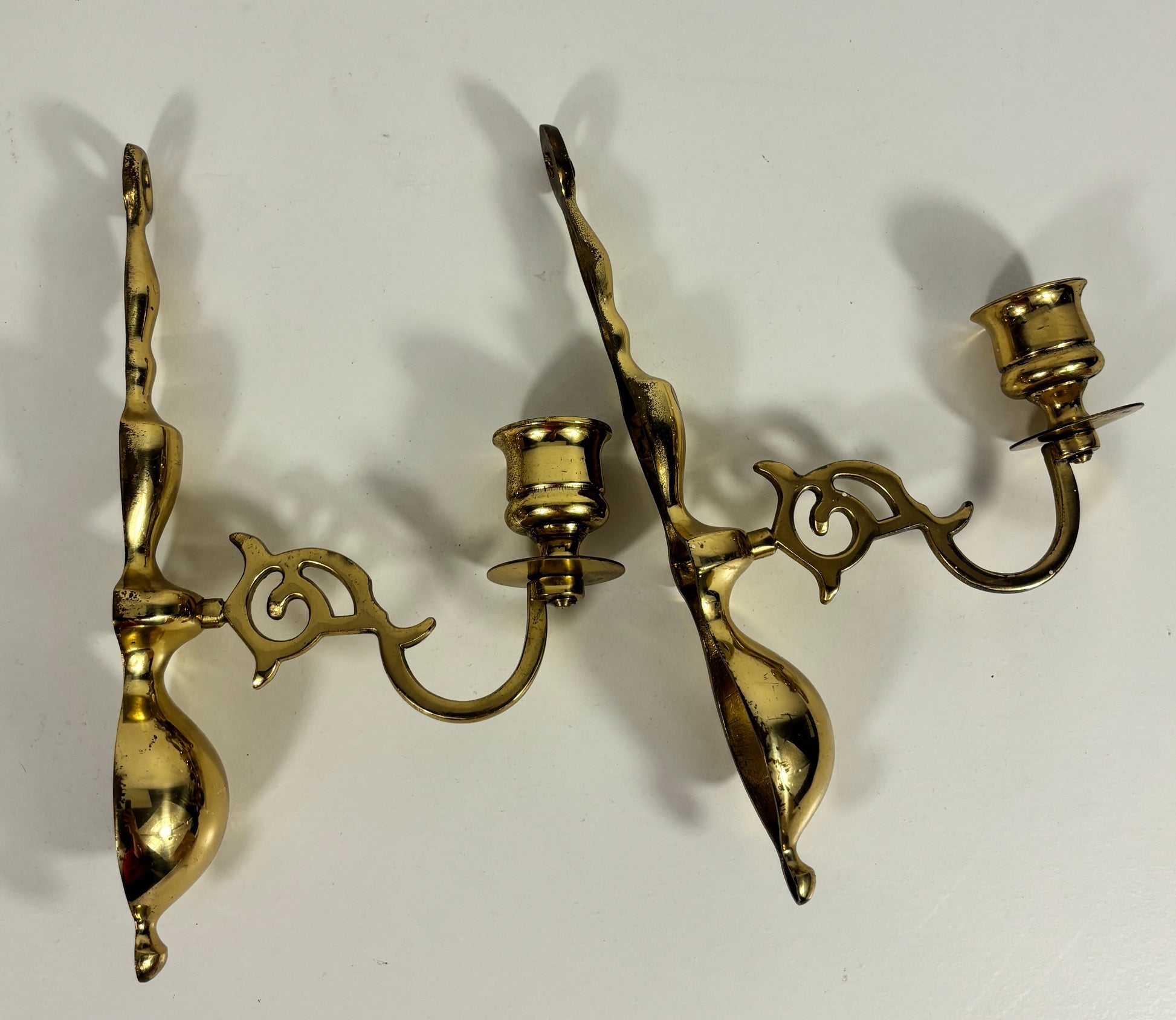 A pair of ornate brass wall sconces with three candle-style lights each, displayed against a plain off-white background.