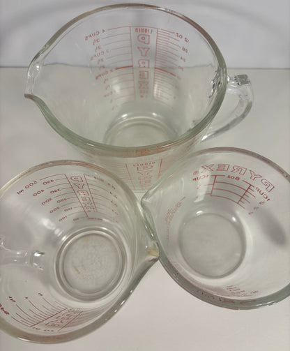 Three clear glass measuring cups with red measurement markings, arranged in a triangular formation on a white background.