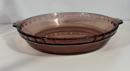 A round, oval-shaped glass pie dish in a translucent smoky brown color, featuring a decorative embossed pattern around the rim and small side handles, set against a plain light background.