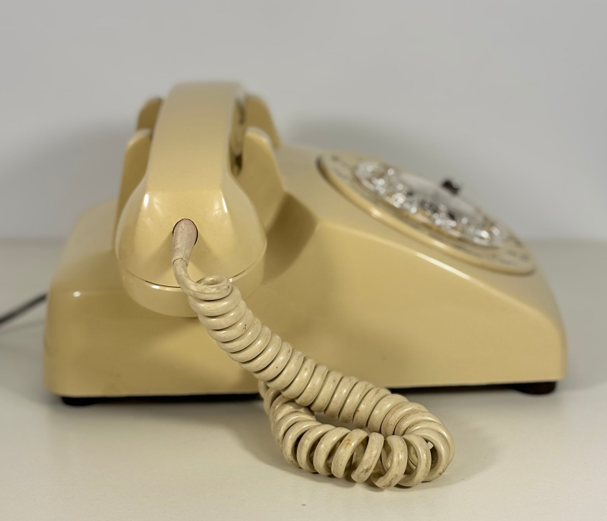 Beige rotary phone with coiled cord on a white background