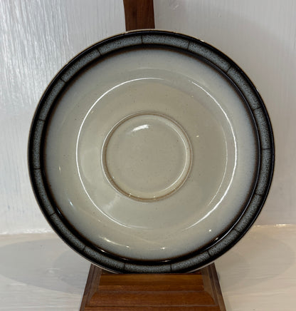 Ceramic saucer with black rim on a wooden stand against a white background