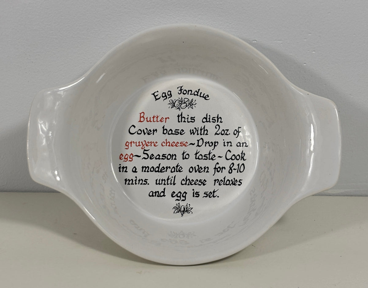 A white ceramic Egg Fondue dish with printed instructions on the inside, photographed against a neutral light gray background.