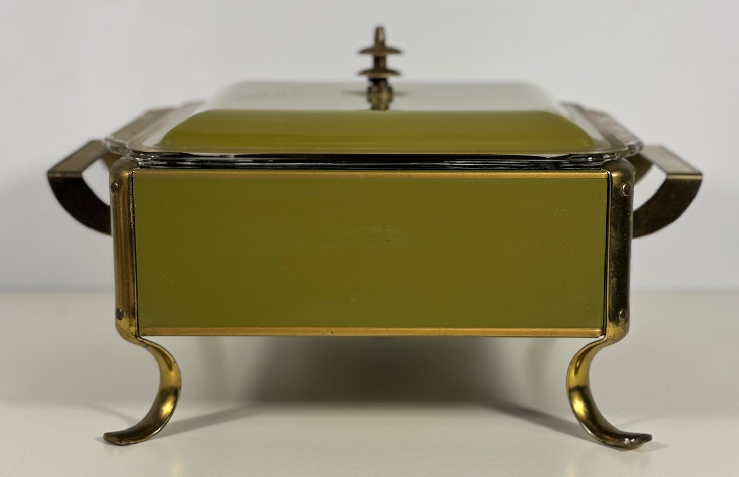An olive green enamel-covered rectangular serving dish with gold-toned metal legs and handles, shown on a plain white background.
