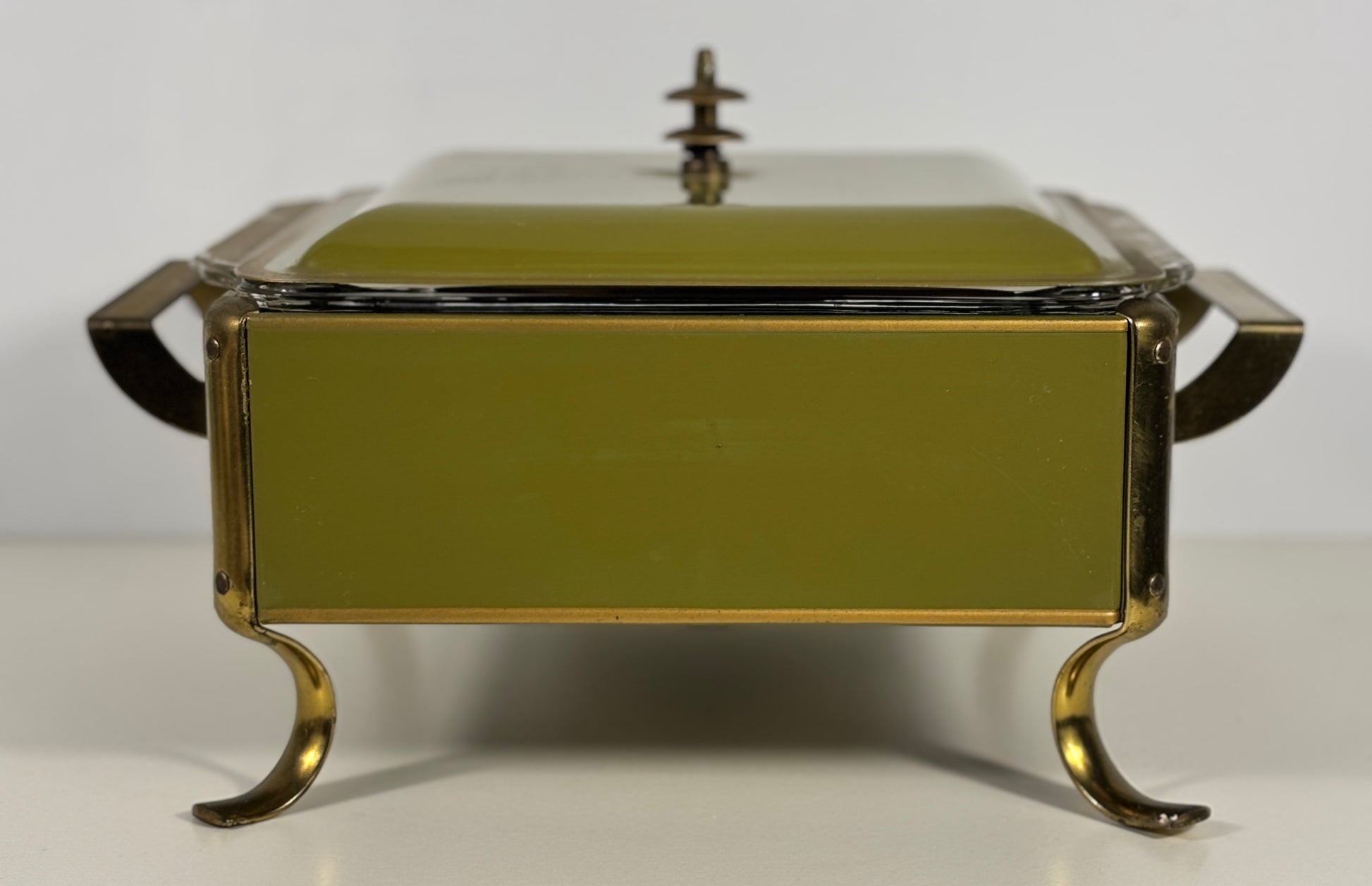 An olive green enamel-covered rectangular serving dish with gold-toned metal legs and handles, shown on a plain white background.