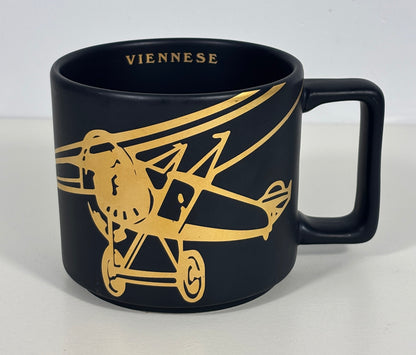 A black ceramic coffee mug featuring a gold-colored graphic of a vintage biplane and the word 'VIENNESE' printed inside the rim, set against a plain light background.