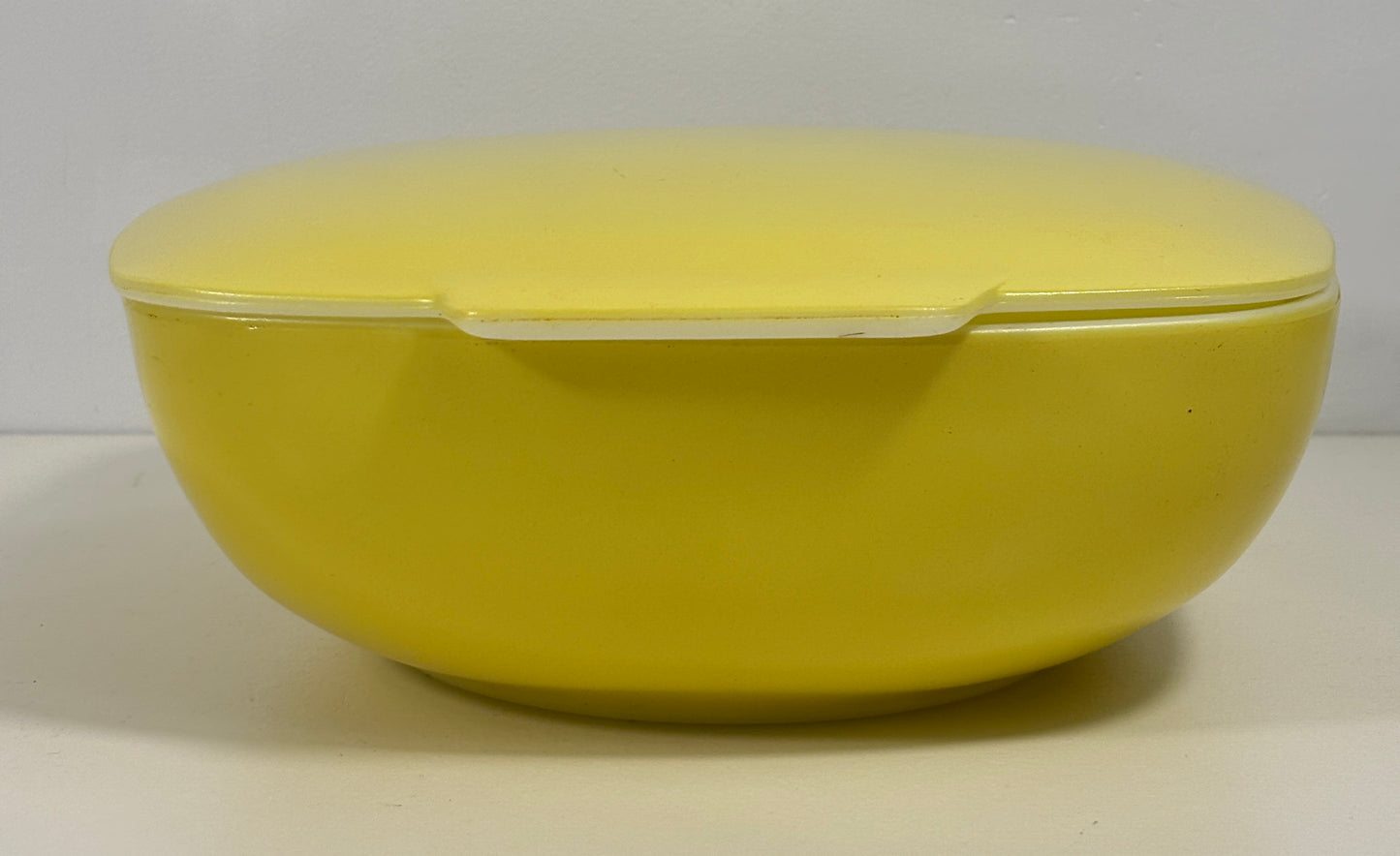 A bright yellow oval lidded container or bowl with a smooth matte finish, photographed against a plain light gray background.