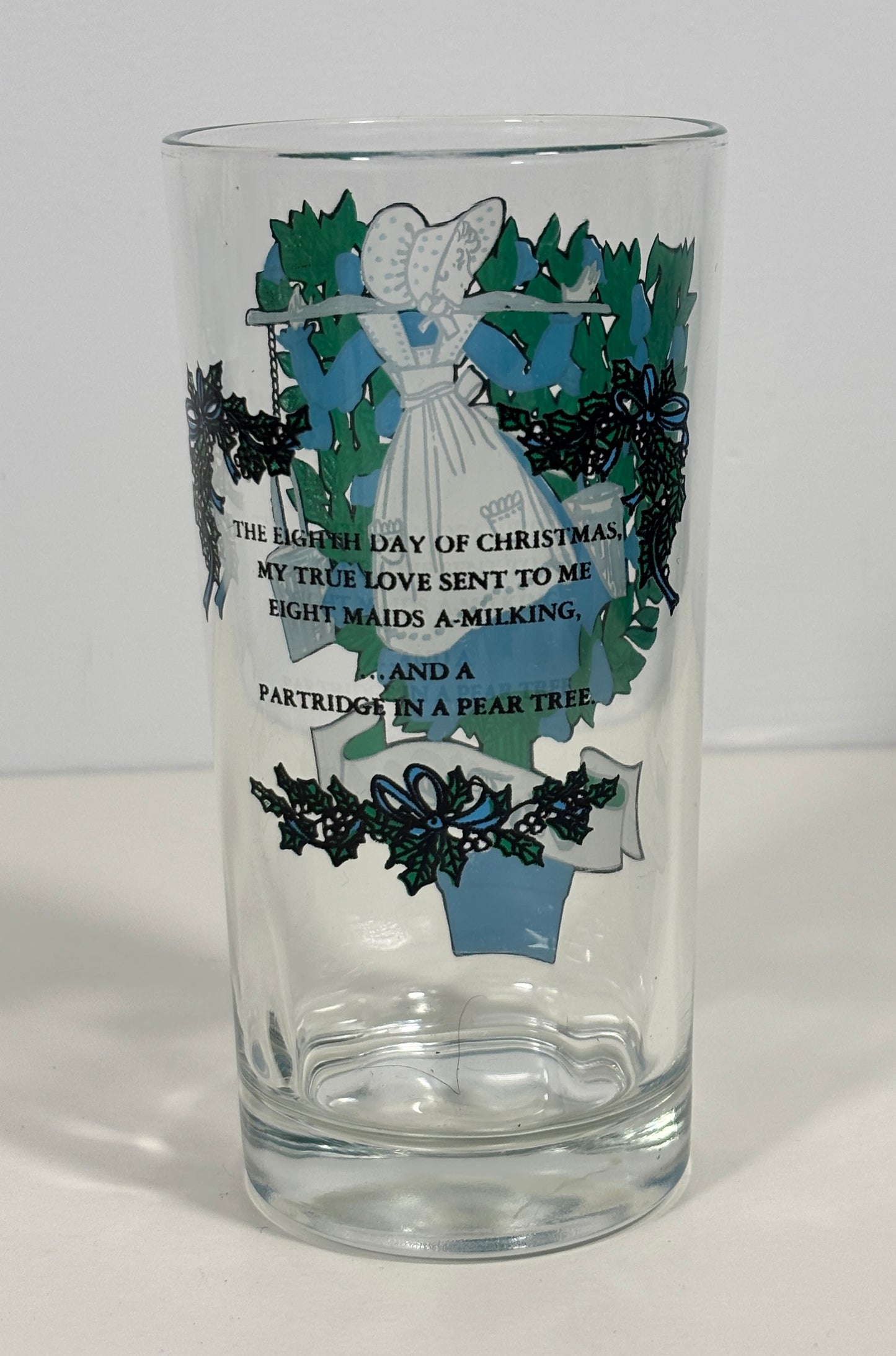 A clear glass drinking tumbler with a Christmas-themed printed design featuring an angel, holly, mistletoe, and a poem about Christmas.