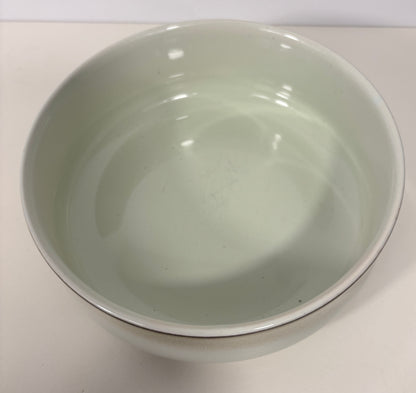 A light green glazed ceramic bowl with a thin dark rim, photographed from a top-down perspective on a plain off-white surface.