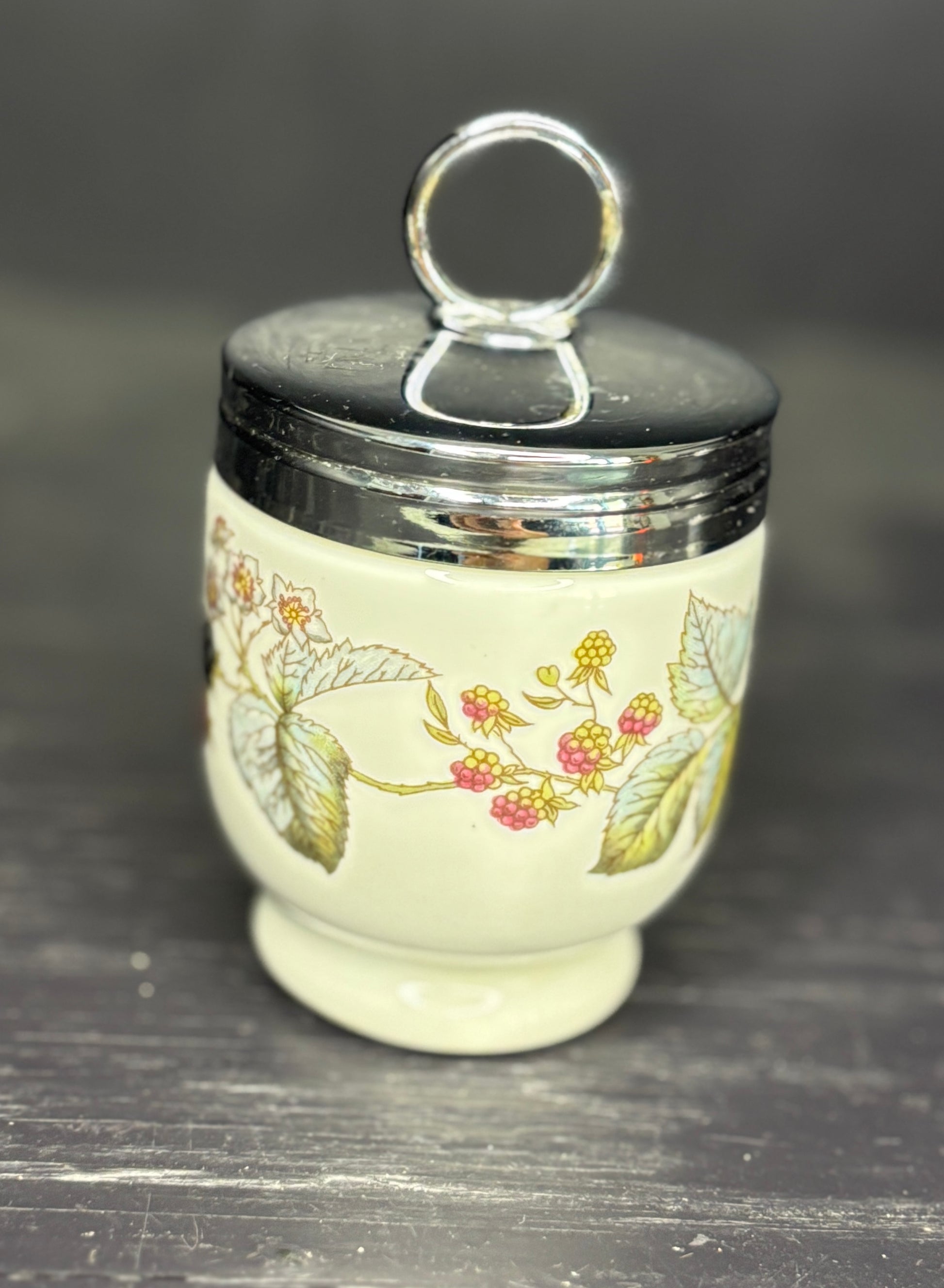 Decorative ceramic jar with floral patterns and a silver lid on a dark surface