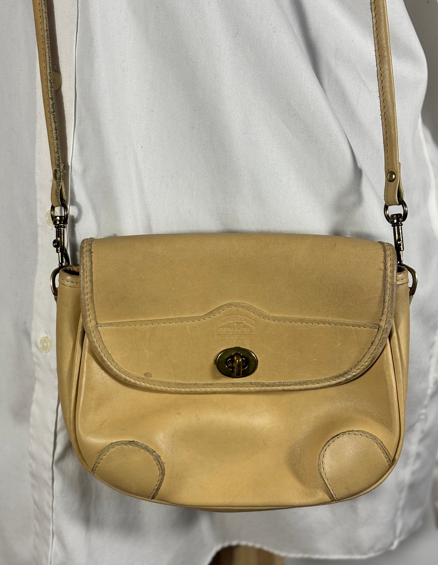 Beige leather handbag with a metal clasp on a light gray background