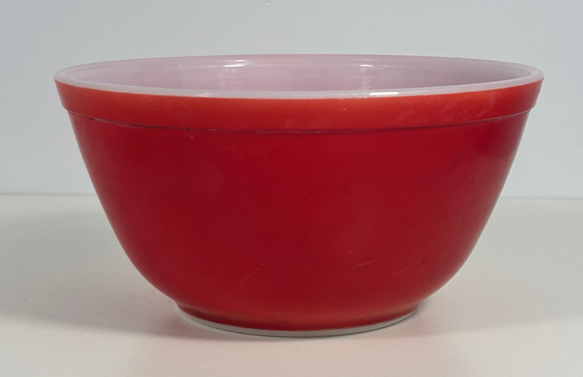 A vintage red glass mixing bowl with a light pink interior, photographed against a neutral light gray background.