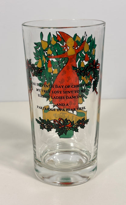 A clear glass pint glass featuring a Christmas-themed illustration of a red cardinal surrounded by green holly leaves and yellow ornaments, with printed text on the front.