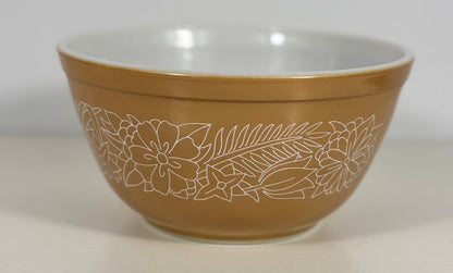 A brown mixing bowl with a white interior and a white etched floral pattern on the exterior, set against a plain light gray background.