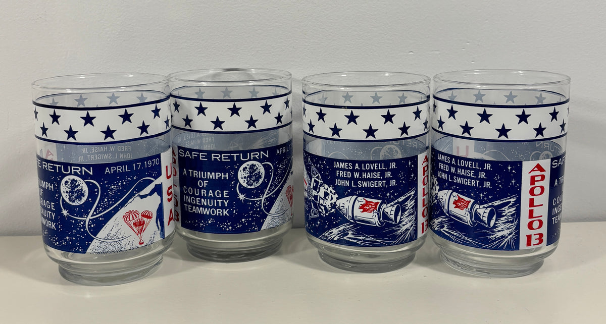 Four clear glass tumblers with blue and white space-themed designs celebrating the Apollo 11 moon landing, displayed side-by-side against a plain light background.